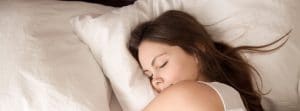 young woman sleeping well in bed hugging soft white pillow