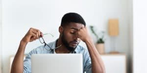 Tired african american employee having headache after working on laptop in office, copy space